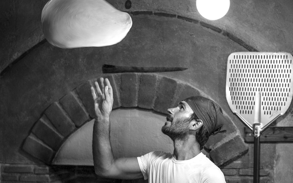 A pizza maker tossing a ball of pizza dough into the air.