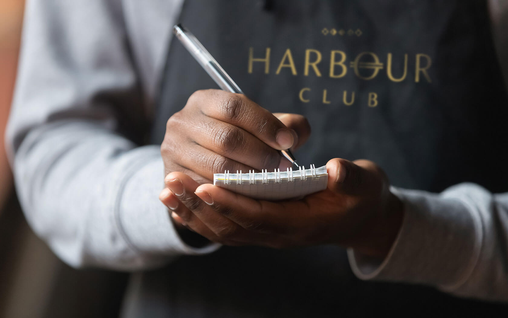 Harbour Club. Image with a waiter writing order on the notepad